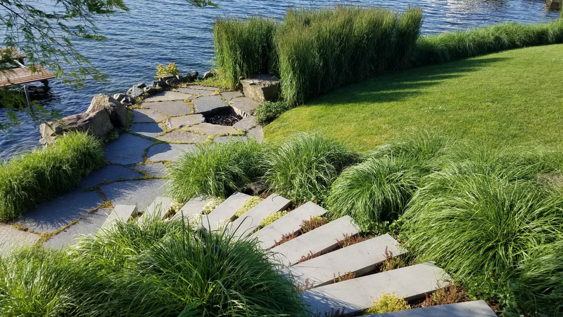 A stone path near the water with grass growing on it.